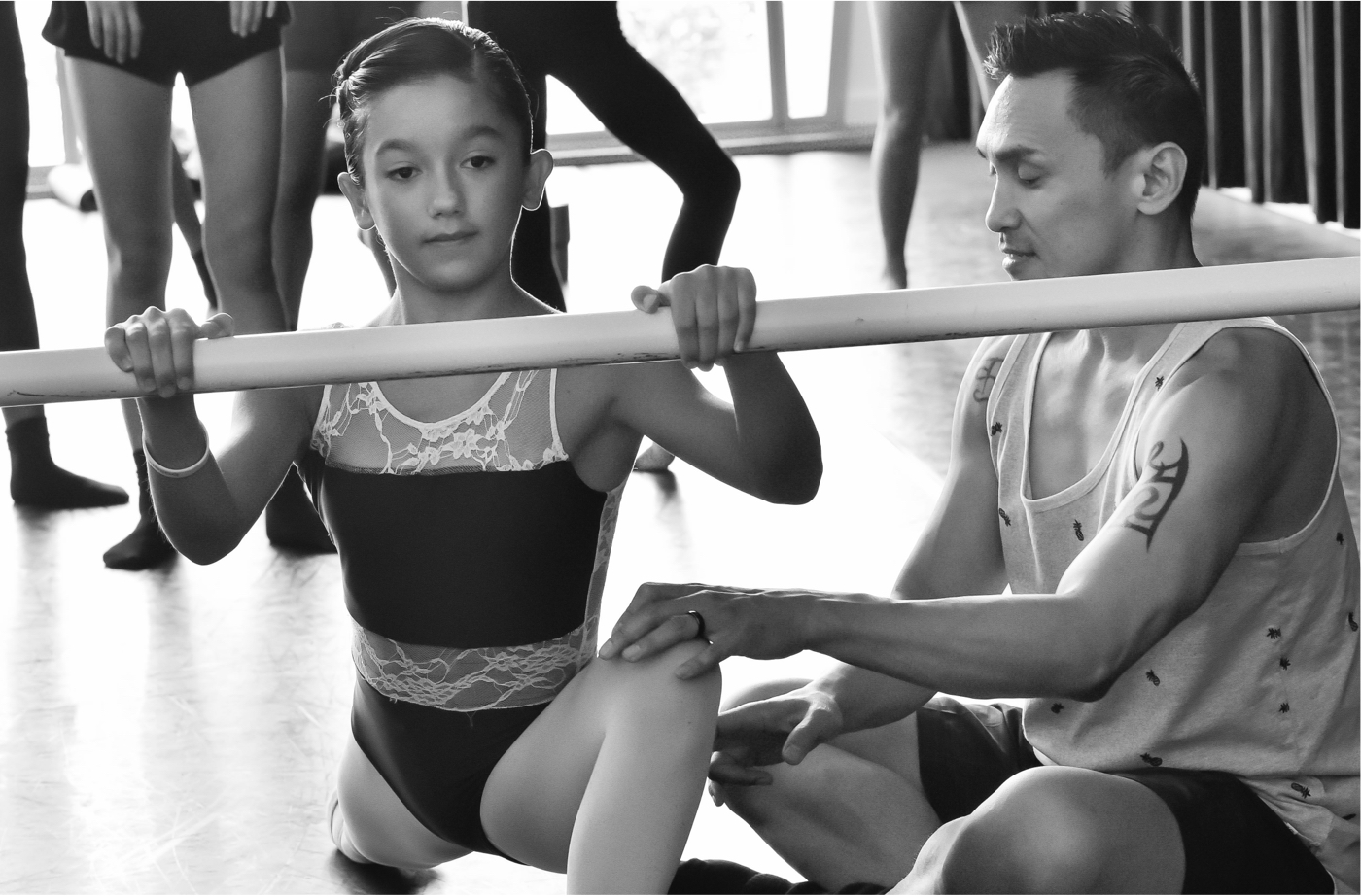 Francisco Gella helping a young dancer stretch at the barre.